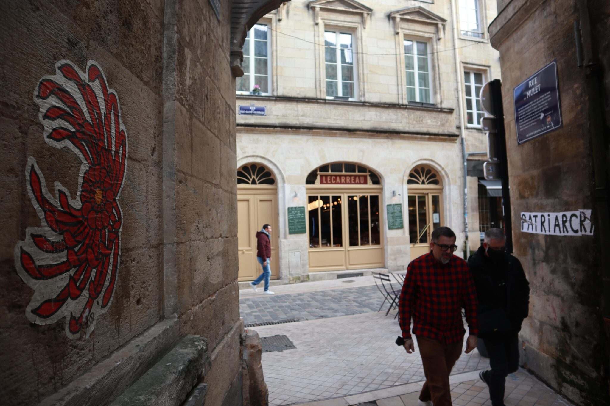 Un chrysanthème rouge collé sur le mur de la rue Mullet à Bordeaux fait face au collage incomplet “patriarcr[...]”.  Art urbain mais aussi outil militant, le collage féminisme est né à Marseille en 2019 pour sensibiliser aux féminicides. Il a aujourd’hui gagné de nombreux pays, et permet de  dénoncer les violences faites aux femmes ainsi que d’autres luttes sociales, LGBTQIA+ ou antiracistes.